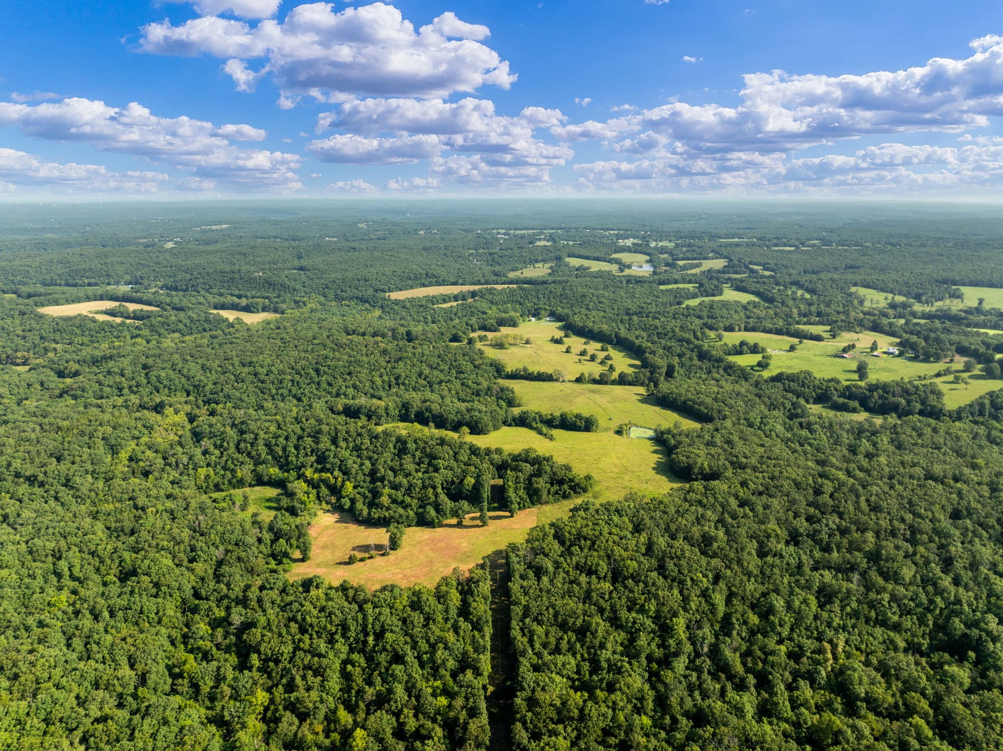 Aerial across pasture, timber, and distant ridges