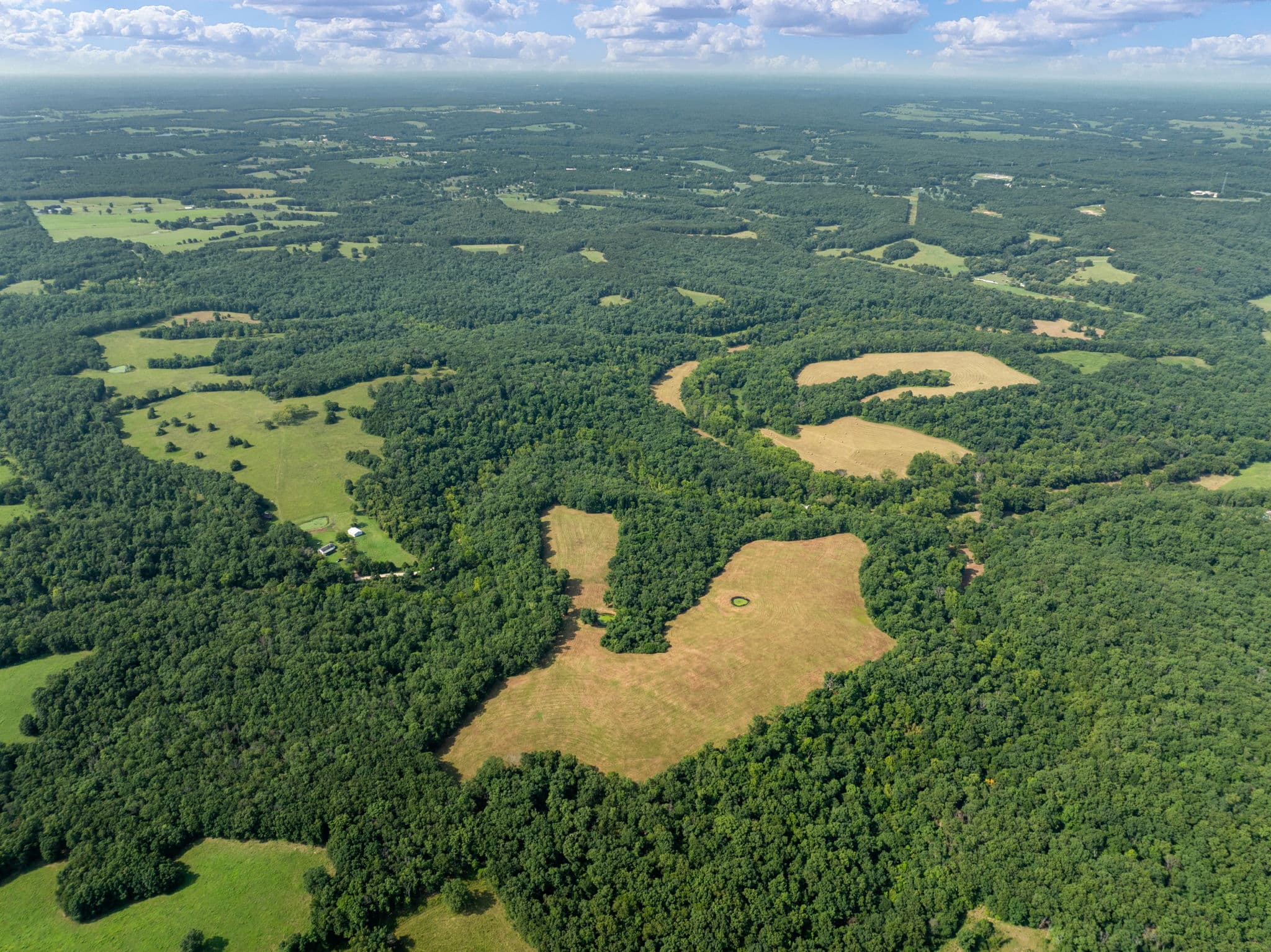 Aerial of open hay ground bordered by hardwoods