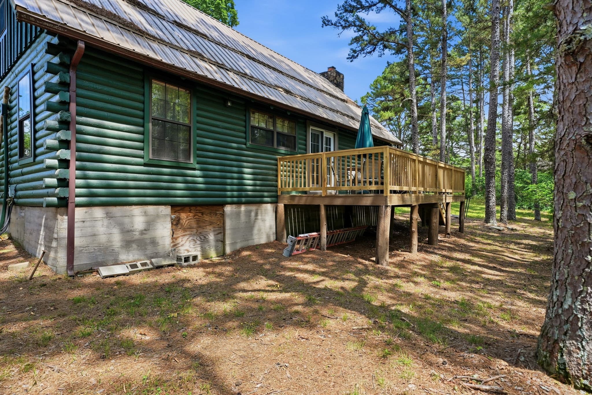 Green log cabin with wraparound deck in the woods